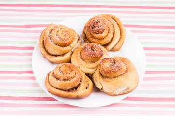 Obraz na płótnie Canvas Freshly baked homemade snail buns with sugar and cinnamon on white plate and striped tablecloth. Balanced nutrition, proteins and carbohydrates, cereals