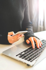 a girl holds a phone in her hand, a laptop stands next to her and glasses lie