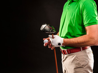Closeup of a male golfer holding a golf ball, a golf iron and wearing a white golf glove....