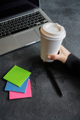 girl holds a coffee mug, a laptop stands next to it and stickers lie