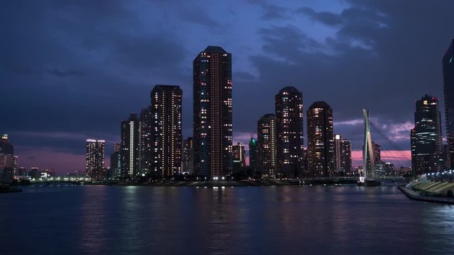 Tokyo skyline at dusk, modern Tsukishima district with scenic water reflection in Sumida river waters. 4K time-lapse