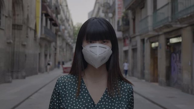 In a pandemic emergency a japanese girl wears a mask while walking through Barcelona city 4K