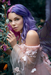 Art photo of a little fairy with pink hair in a fairy forest among flowers