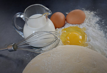Appetizing still life of flour, eggs, a whisk, a jug of milk and dough