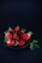 Fresh juicy strawberries in a black plate on a black matte background
