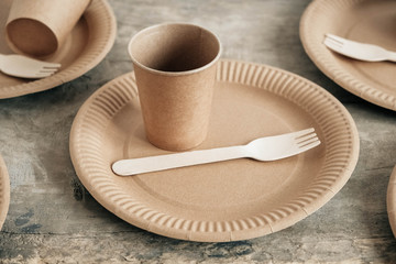 Wooden forks and paper cups with plates on wooden background. Eco friendly disposable tableware. Also used in fast food, restaurants, takeaways, picnics. Copy, empty space for text