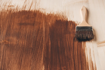 Paint brush with wooden handle and natural bristles against the background of painted brown wooden...