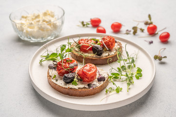 Fototapeta na wymiar Homemade sandwiches with baked tomatoes, olives, cheese and herbs on bread on a white ceramic plate