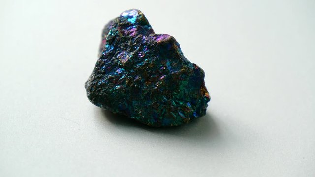 Natural multi-colored green blue chalcopyrite stone spins around its axis on a white stand and white background. Gems, minerals, collection of natural stones, close-ups, study of minerals