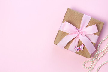Gift box with a pink bow and pearl beads on a pastel pink background. Flat lay style.