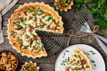 Homemade quiche or tart with chanterelles on an old wooden background. A slice of tart on a plate. Rustic style. Top view - obrazy, fototapety, plakaty