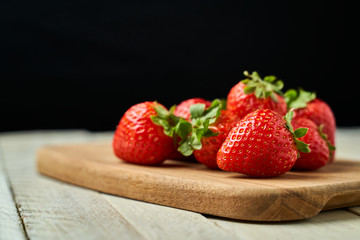 Red strawberries on a wooden board with a dark background.