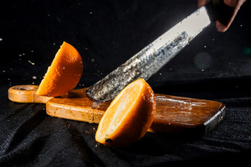 Orange are chopping by machete on wooden desk at black isolated background