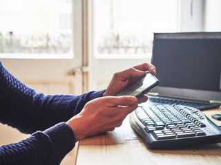 Close-up image of a man working at home with his computer and cell phone in hand.