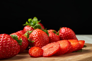 Freshly cut red strawberries on a wooden board with a dark background.