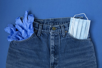 Classic blue jeans on the white background. Medical mask in the pocket. Pandemic concept. Top view. Flat layout