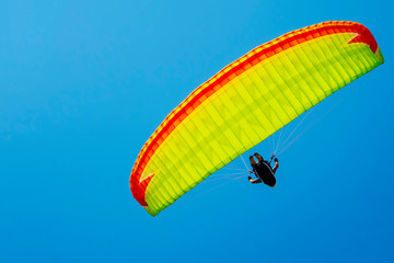 Yellow paraglider with a pilot on a bright blue sky background. Copy space.