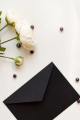 Business concept. Gift concept. On a white table is a black cider envelope and a rose branch with beads. Close-up.