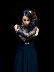 Mystical lady in a black dress with makeup with flowers in her hair on a black background. Magic black, Gothic beauty, mystical image