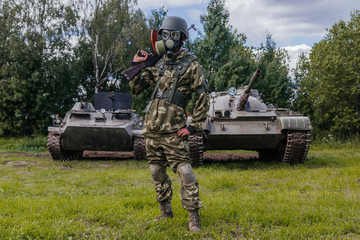 A soldier in a gas mask with a Kalashnikov rifle against the background of armored vehicles.