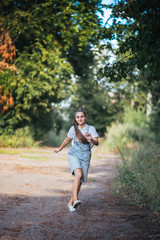 A girl in denim overalls smiles and runs outdoors.