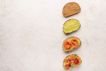 Stages of making a sandwich of bread, guacamole, salted salmon, baked tomatoes and greens
