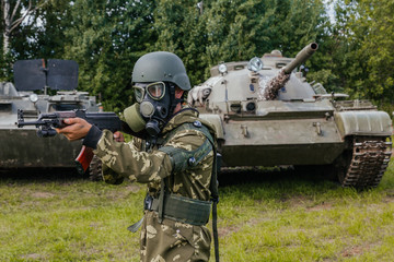 A soldier in a gas mask with a Kalashnikov rifle against the background of armored vehicles.