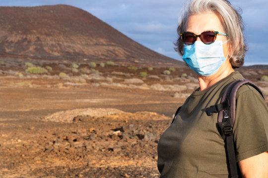 Senior woman with medical face mask enjoys nature outdoors in the mountains. Partial conquest of freedom after coronavirus lockdown