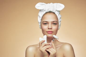 Girl in bandage on head uses beauty gua sha jade quartz roller. Satisfied smile. Perfect glowing...