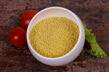 Raw couscous in the bowl served salad leaves, tomato and pepper