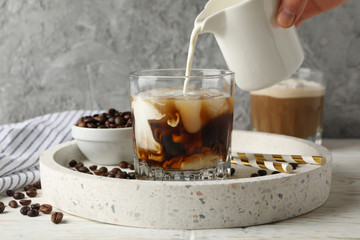 Woman pours a milk in glass of coffee. Composition with ice coffee