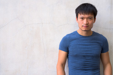 Portrait of young Asian man against concrete wall