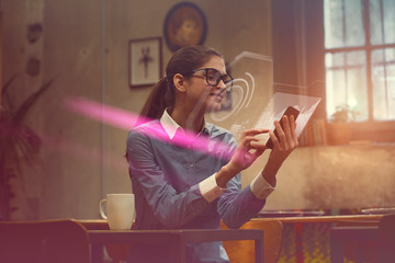 Using high end technology in a world still trying to catch up. A beautiful young woman is analyzing data and graphic charts from her phone, projected into holograms in front of her phone's screen.