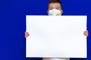 Close up Portrait of caucasian boy in a protective mask respirator holds a blank sheet of paper on...