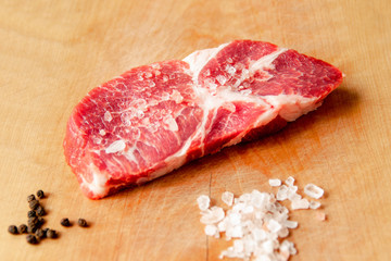 A piece of steak lies on a cutting board, next to salt, pepper.