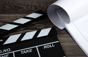 black movie clapper with a script sheets on a wooden table