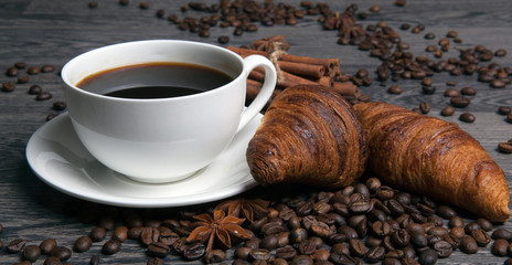 cup of hot coffee and roasted coffee beans with toasted croissants