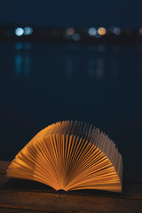 Open book at a sea port at night with a nightlight. Concept: Leasure night reading at the beach