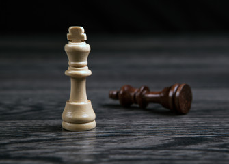 the white king defeats the black king in chess on a wooden table