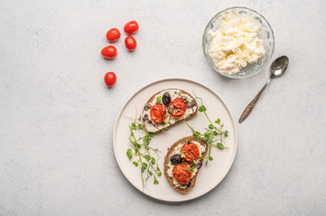 Homemade sandwiches with baked tomatoes, olives, cheese and herbs on bread on a white ceramic plate