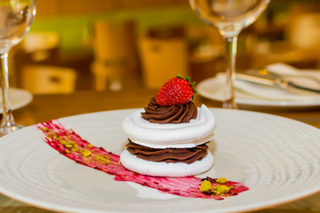 Meringue cake with dark chocolate and strawberry on top, in arestaurant setting, blurred background