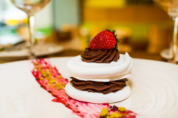 Meringue cake with dark chocolate and strawberry on top, in arestaurant setting, blurred background