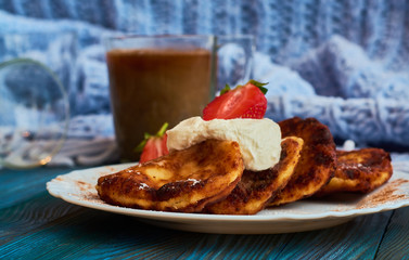 Delicious and useful breakfast of cheese pancakes with sour cream and strawberries cooked at home, with strong black coffee on blue background of wood and plaid.