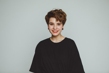 A girl with short hair stands on a white background and smiles