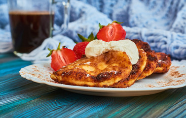 Delicious and useful breakfast of cheese pancakes with sour cream and strawberries cooked at home, with strong black coffee on blue background of wood and plaid.