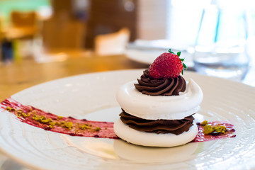 Meringue cake with dark chocolate and strawberry on top, in arestaurant setting, blurred background