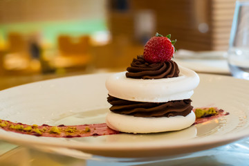 Meringue cake with dark chocolate and strawberry on top, in arestaurant setting, blurred background