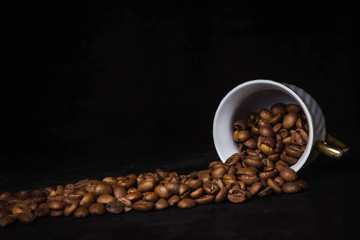 Coffee scattered in a row on a black background. Nearby lies a coffee cup.