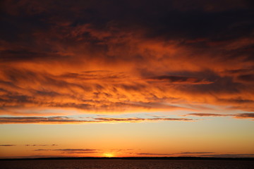 A fire is burning in the sky at sunset with lush illuminated orange clouds covering half of the clear horizon.The last glimmer near the lake.A striking contrast picture at the end of the day.Russia