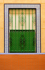 Green painted iron window with Triana tile perimeter frame, white plastic shutter and wooden latticework. Facade of a house in a popular neighborhood of Seville, Spain
